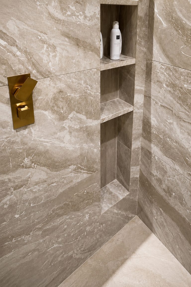 Stone tiled shower niche with brass control plate and large format wall tiles