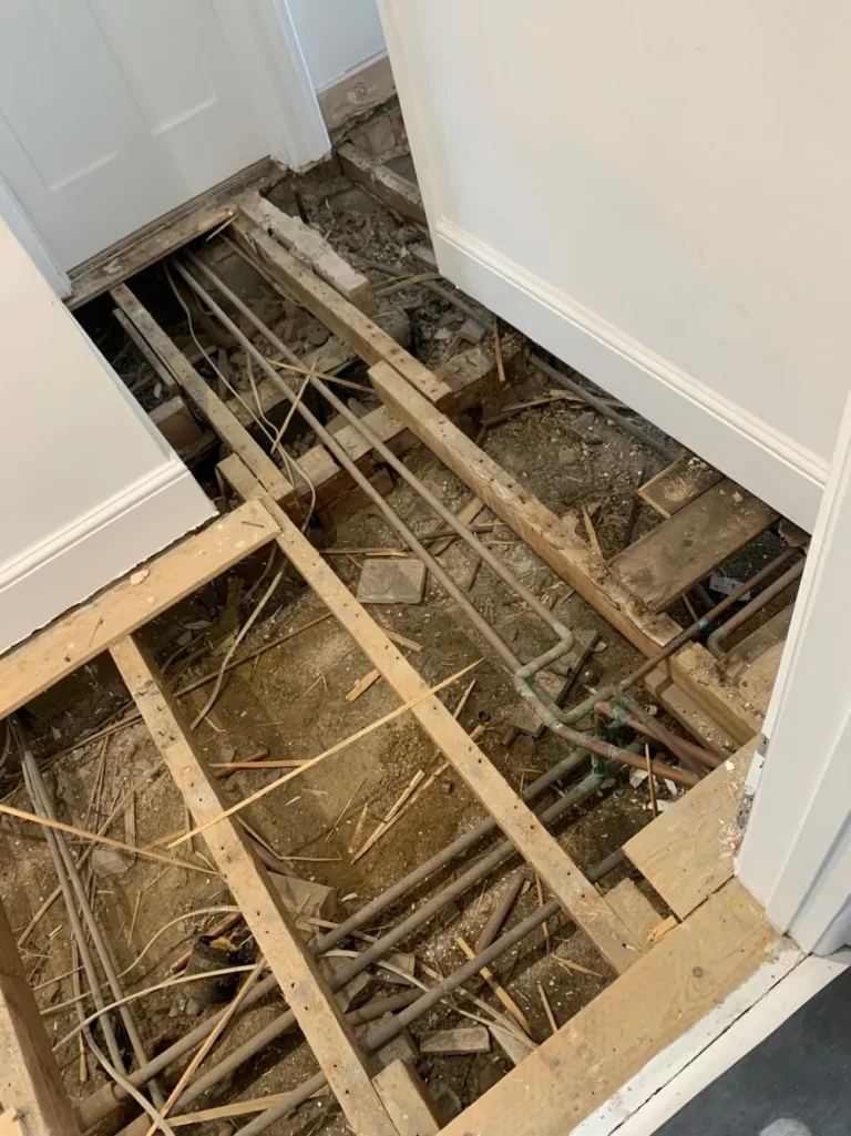 Open suspended timber subfloor with joists, pipework and services exposed before reinforcement.